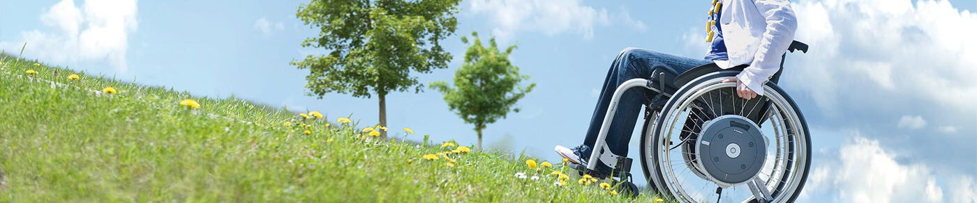 E-Motion Greifreifenantrieb Layout Seitenkopf  E-Motion Person mit Rollstuhl fährt eine Berg h och