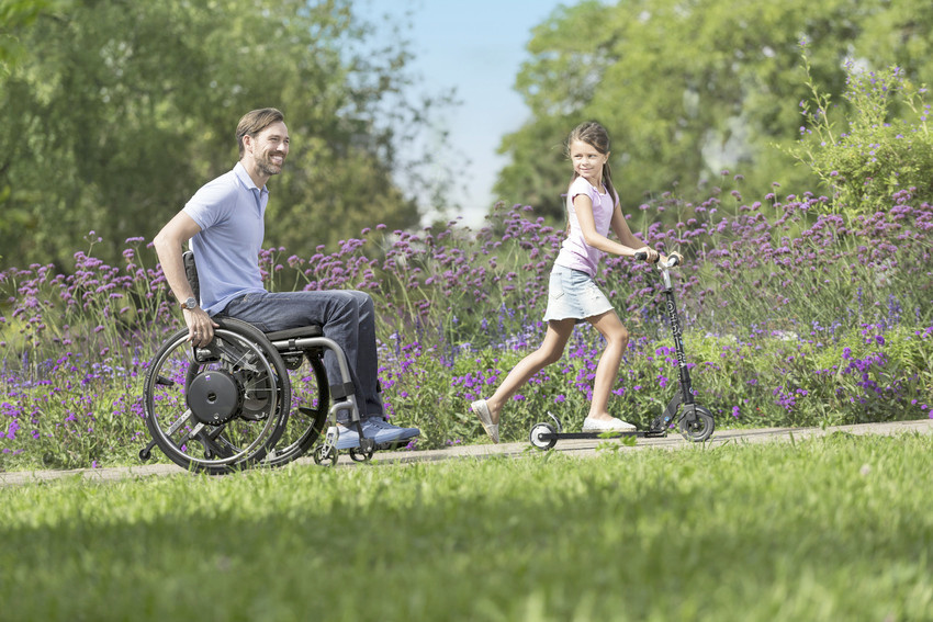 E-Motion BE 130 Ansteigender Feldweg, eine Person im Rollstuhl mit E-Antrieb und ein Kind mit Roller