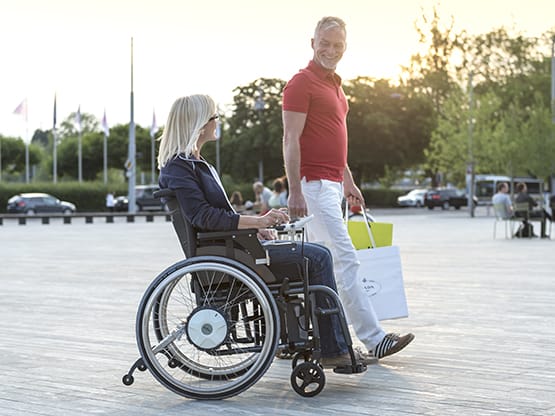 Alber Zusatzantrieb E-Fix Zwei Personen nach dem Einkaufsbummel, eine Person im Rollstuhl mit E-Fix Zusatzantrieb