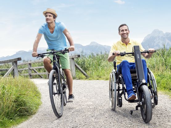 E-Pilot Zuggerät für manuelle Rollstühle Fahrradfahrer und Rollstuhlfahrer mit E-Pilot Zuggerät auf einem Radweg in den Bergen